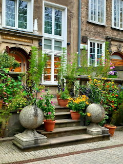 Brick courtyard with potted plants, stone steps, and tall windows in historic Gdańsk building