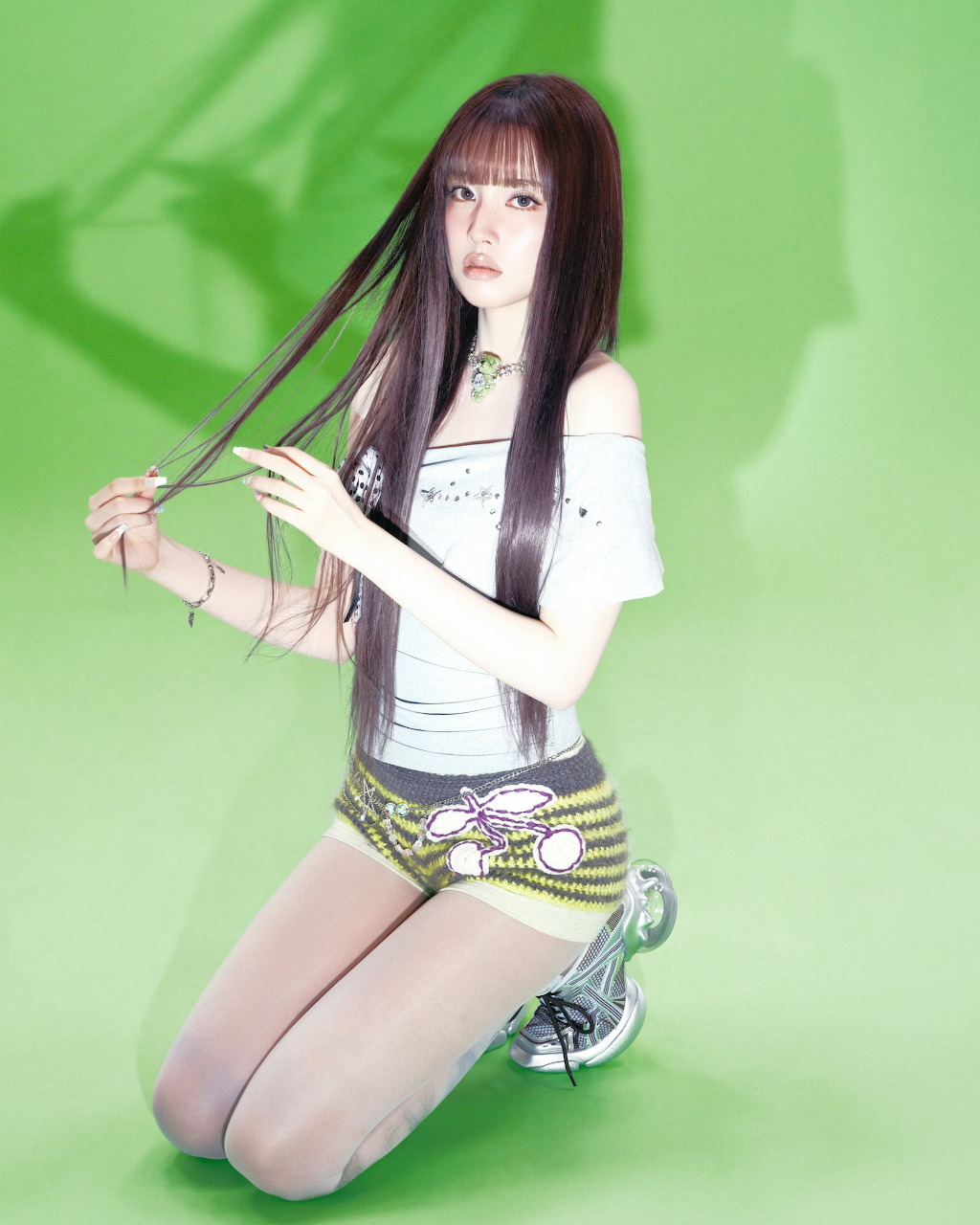 Illustration of woman with long dark hair kneeling against green backdrop, wearing white top and denim shorts