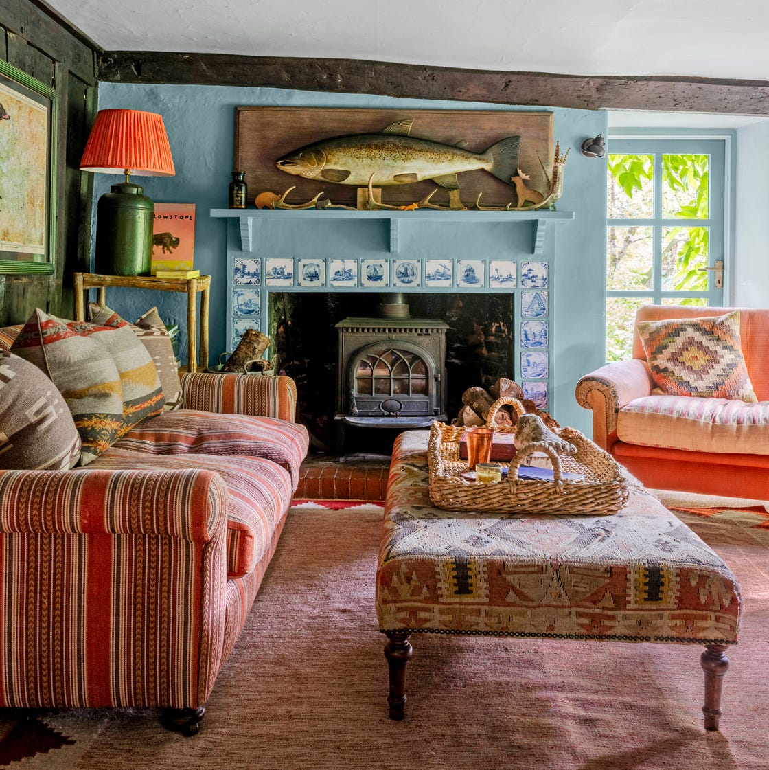 Cozy cottage living room with pink striped sofa, fireplace, wicker table, and mounted fish decoration above mantel