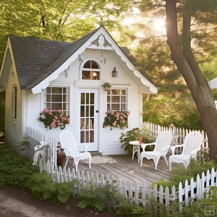 White cottage with arched door, window boxes, white picket fence, and garden in forest clearing