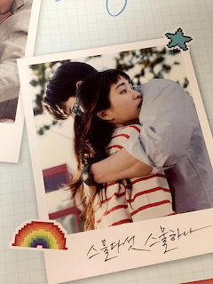 Polaroid photo of a young Asian couple hugging, with rainbow and star pixel stickers and Korean text