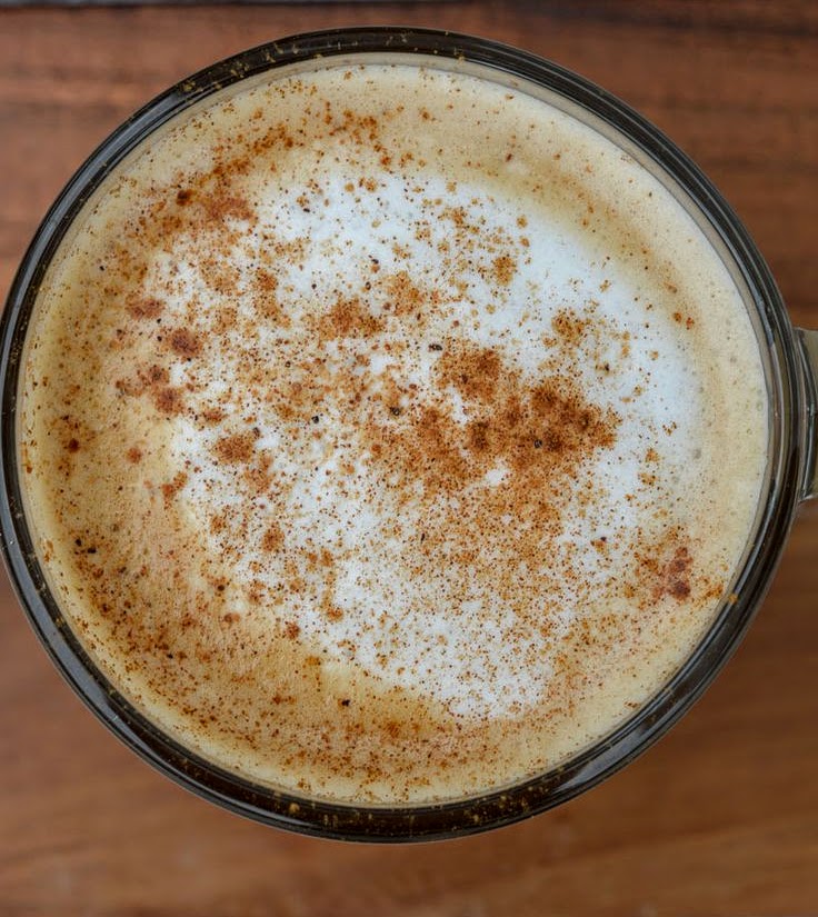 Top-down view of a latte with spiced foam in a glass mug on wood