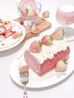 Pink layered cake roll topped with strawberries and cream on white plate