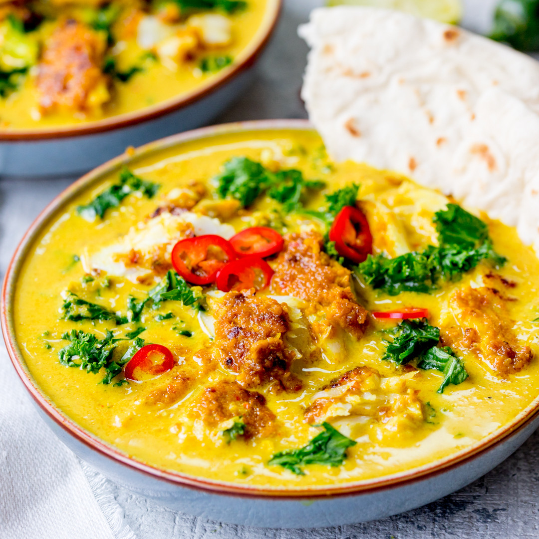 Bowl of yellow curry with red chili slices, fresh herbs, and flatbread beside it