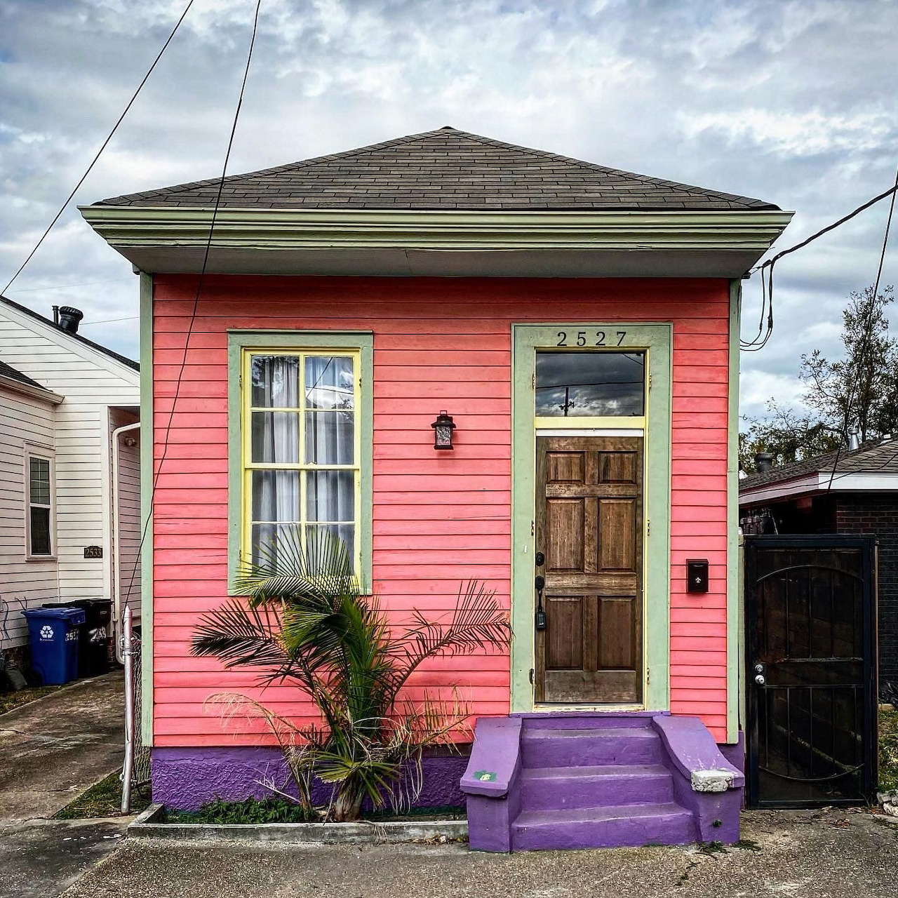 Bright pink tiny house with purple steps and brown door in residential neighborhood