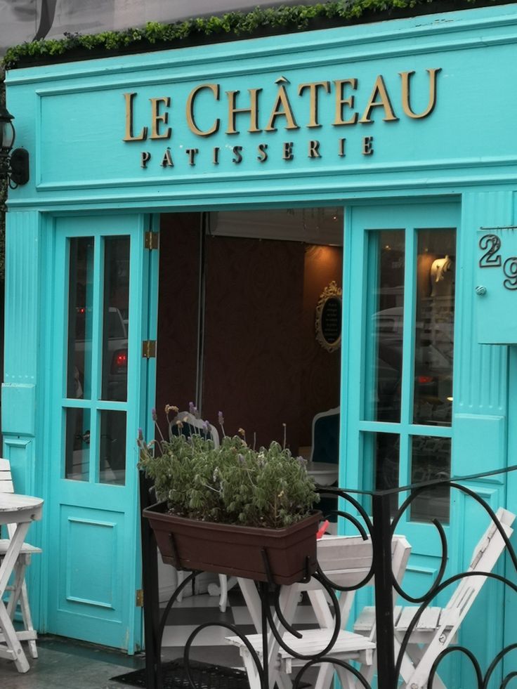 Turquoise Le Chateau Patisserie storefront with open doors, white chairs, and an outdoor planter