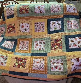 Colorful patchwork quilt with apple motifs and floral fabric squares draped over a chair