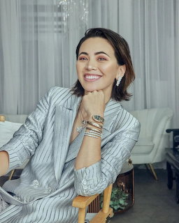 Woman in striped blazer smiling at camera in bright room with white curtains