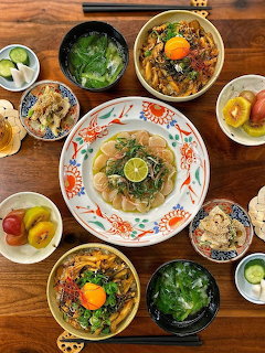 Overhead view of a Korean meal spread with noodles, soup bowls, side dishes, and fruit on a wooden table