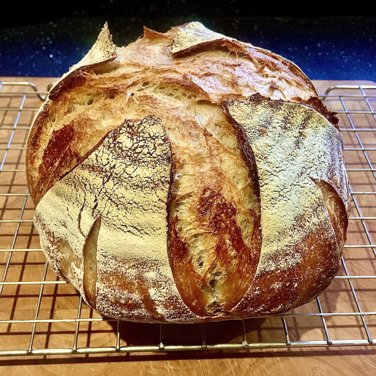 Round sourdough bread loaf with scored golden crust on wire cooling rack
