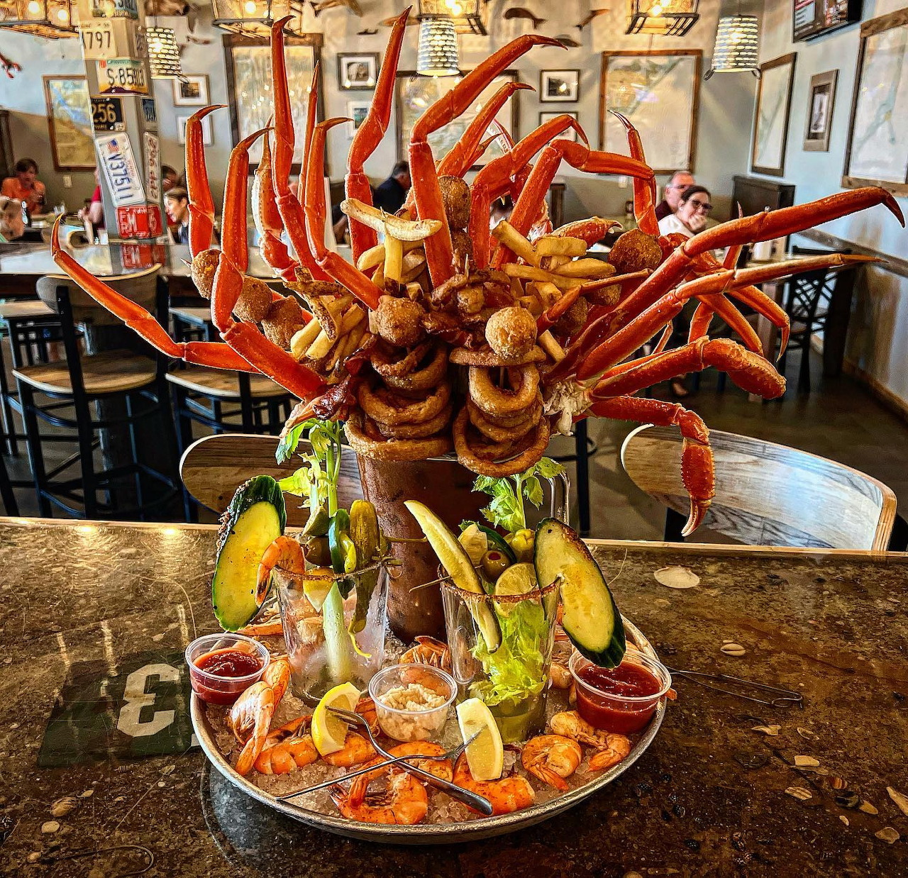 Large Bloody Mary topped with crab legs, shrimp, oysters, and garnishes on a tray in a restaurant