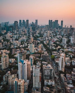 Aerial view of Mumbai skyline with dense high-rise buildings beneath a soft pink sky.