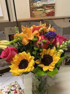Colorful bouquet with sunflowers, orange lilies, pink roses, and purple flowers in a glass vase