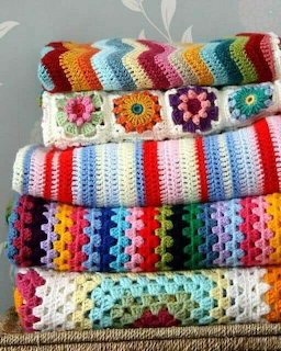 Stack of five colorful handmade crochet blankets with stripes, granny squares, and rainbow patterns