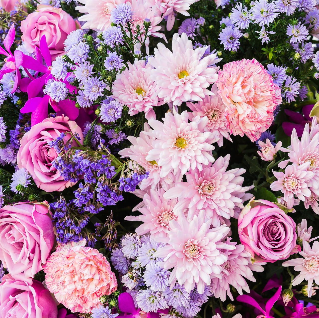 Vibrant mix of pink roses, purple flowers, and pale pink dahlias in a lush floral arrangement