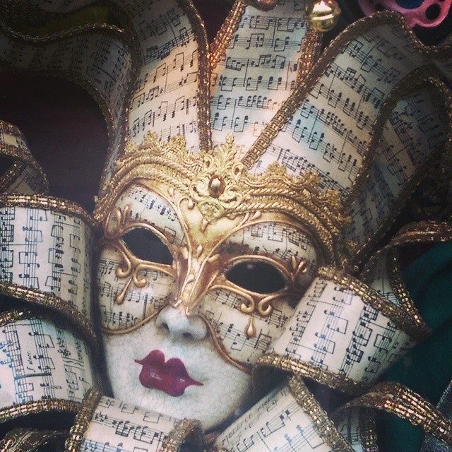 Ornate white mask with sheet music pattern, gold trim, and purple lips