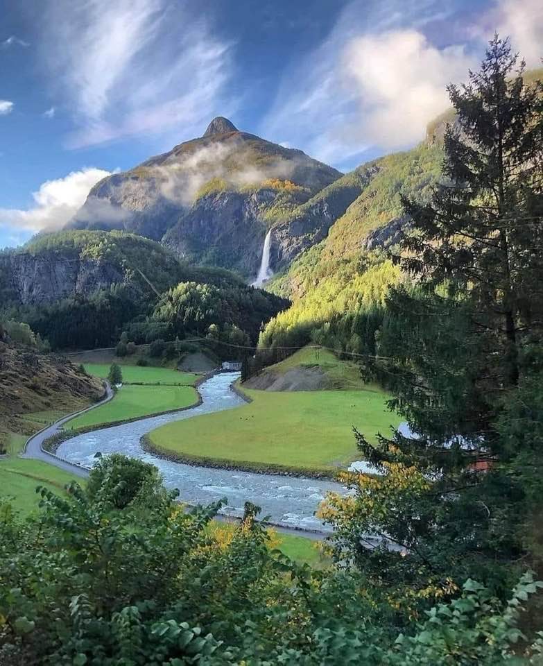 Winding river through green valley with waterfall and mountain peak in Flåm, Norway