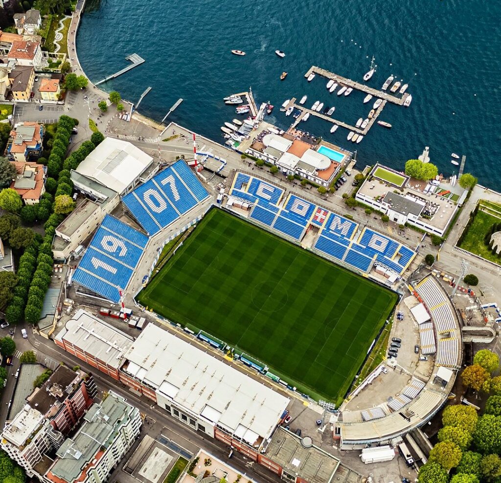 Aerial view of a soccer stadium next to a marina with boats and waterfront buildings