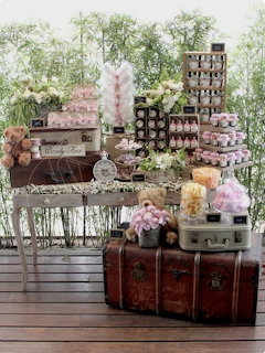 Rustic dessert display with cupcakes, flowers, crates, and vintage suitcases by tall windows