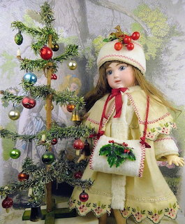 Porcelain doll in vintage yellow coat with white fur trim next to small decorated Christmas tree