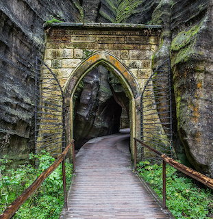 Wooden walkway leading through a stone arch in a narrow rocky passage