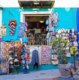 Colorful street shop with blue walls displaying clothing, bags, and souvenirs outside storefront