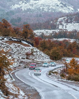 Cars on a winding wet road through snowy hills and autumn trees