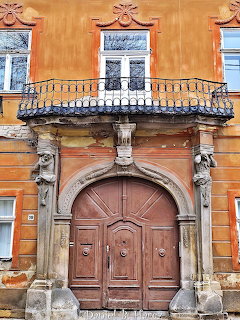 Orange historic building with ornate wooden door, balcony with iron railing, and decorative stone columns
