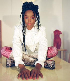 Portrait of woman in white blazer with long braids seated on patterned chair
