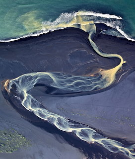 Aerial view of winding water channels on black volcanic sand meeting the sea