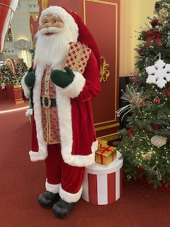 Santa Claus figure in red suit next to Christmas tree with presents