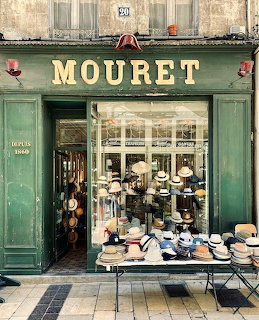 Green-painted Mouret hat shop storefront in Paris with display of various hats on outdoor table