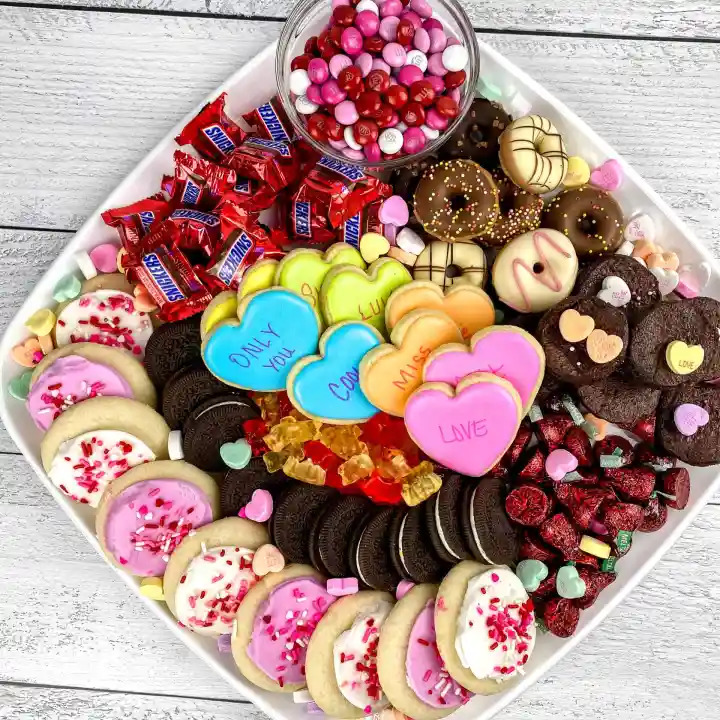 White platter filled with colorful decorated cookies, chocolates, candies and heart-shaped treats on wooden surface