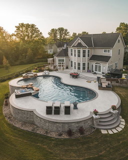 Aerial view of white house with curved pool and patio at sunset