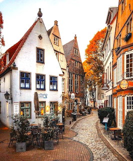 Narrow cobblestone street lined with colorful historic buildings and outdoor café tables in Bremen, Germany