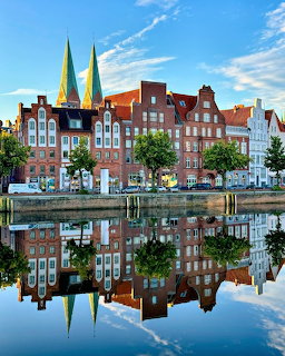 Historic Lübeck waterfront with colorful buildings and green church spires mirrored in a calm canal