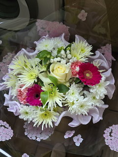 Wrapped bouquet with white roses, pink gerbera daisies, and chrysanthemums on a glass table