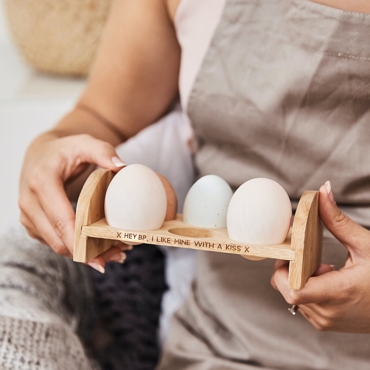 Hands holding a wooden rack with three white eggs