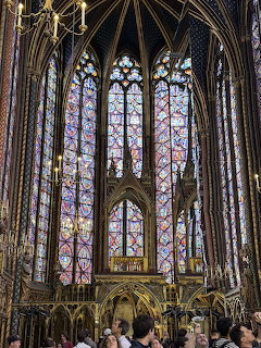 Interior view of Sainte-Chapelle showing tall Gothic stained glass windows with biblical scenes in ornate stone arches