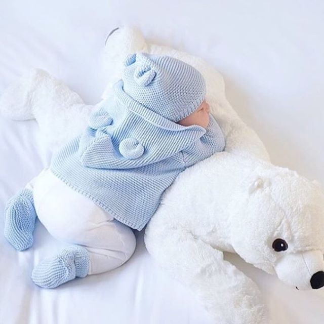 Newborn baby in blue sweater lying next to white teddy bear
