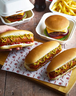 Burgers, hot dogs with toppings, and fries arranged on a wooden table