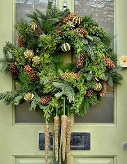 Green Christmas wreath with pine cones and gold ornaments on a light green door