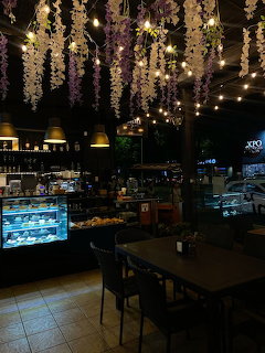 Cafe interior at night with hanging lights, wisteria flowers, display cases and wooden tables