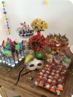 Festive party table with carnival mask, colorful feathers, candy, flowers, and decorations