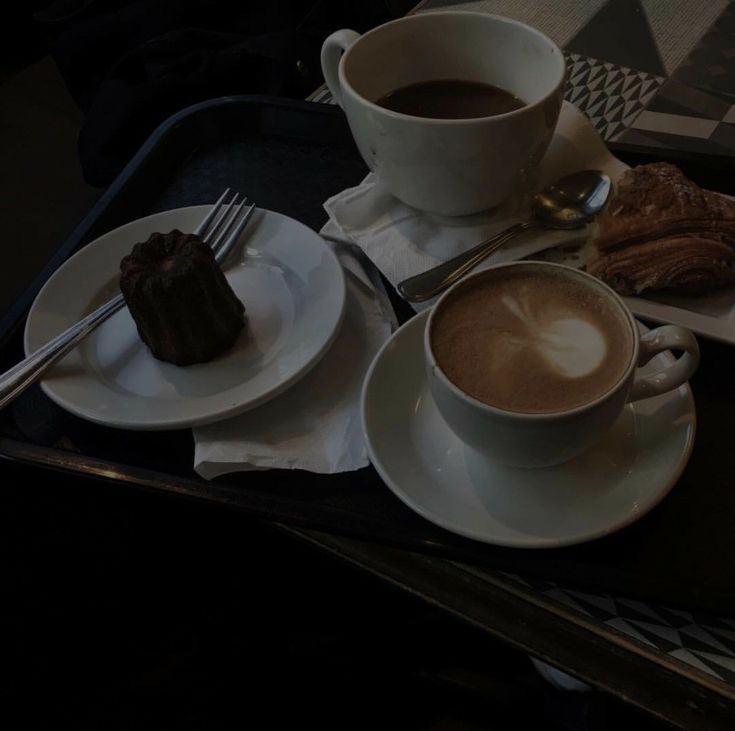 Two coffee cups with latte art and a chocolate dessert on white plates on a black tray