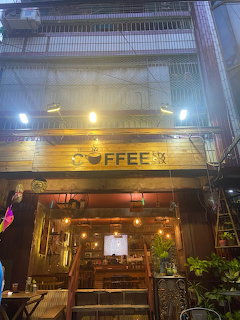 Warmly lit coffee shop storefront at night in a narrow city building