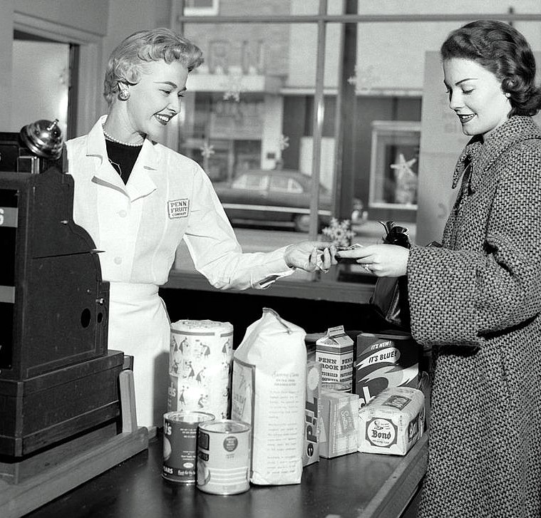 Black-and-white vintage photo of a cashier and customer at a grocery store counter