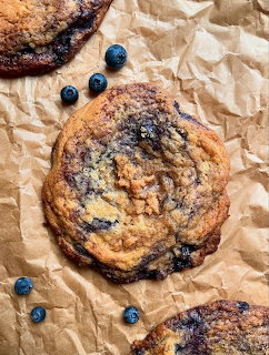 Large blueberry chocolate chip cookie on parchment paper with fresh blueberries scattered around