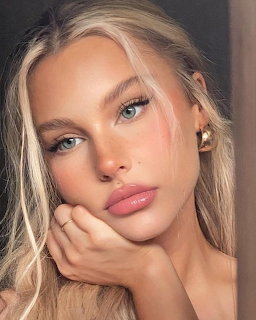 Close-up portrait of a young blonde woman with blue eyes and pink lips resting chin on hand