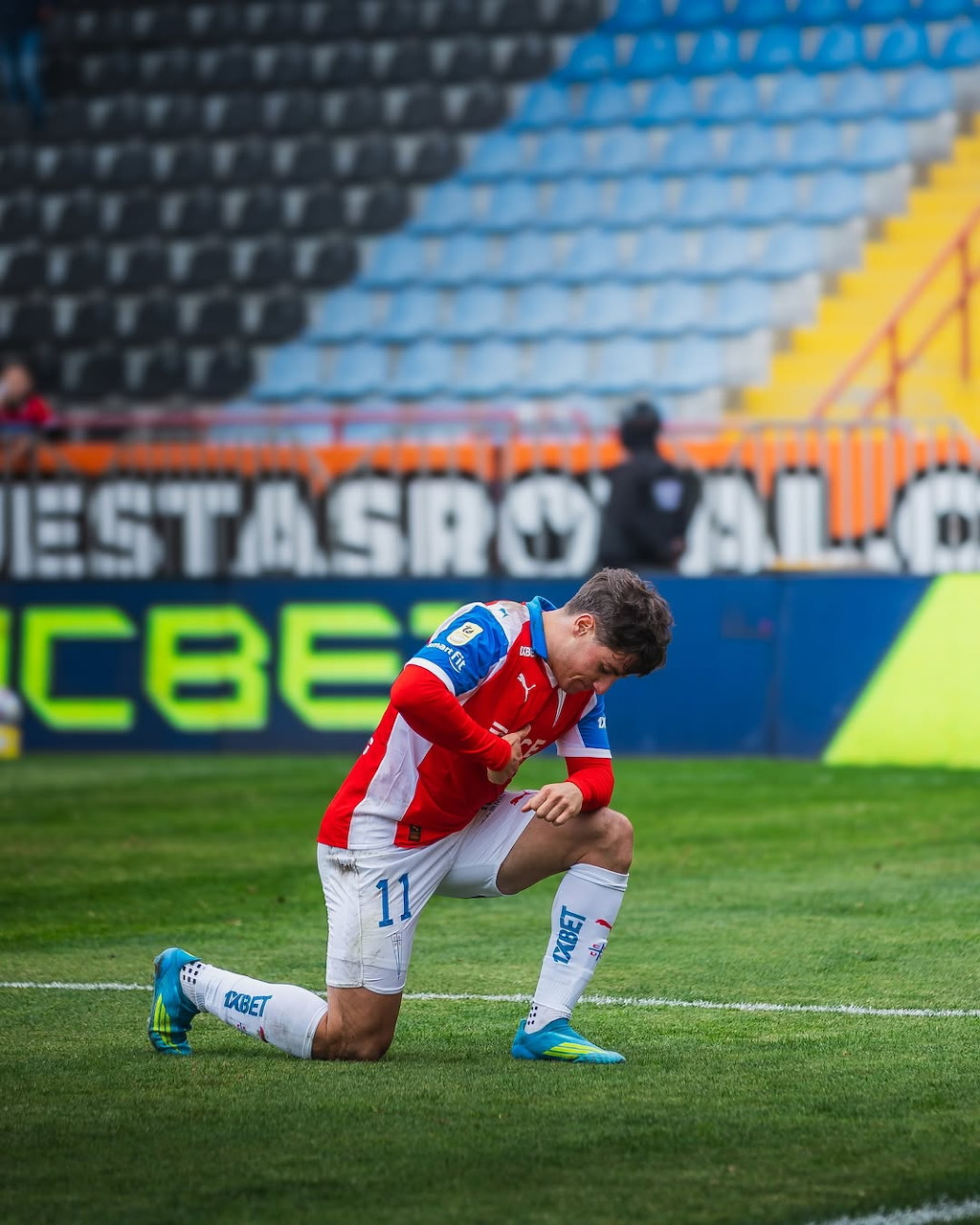 Soccer player in a red and blue uniform kneeling on the field during a stadium match